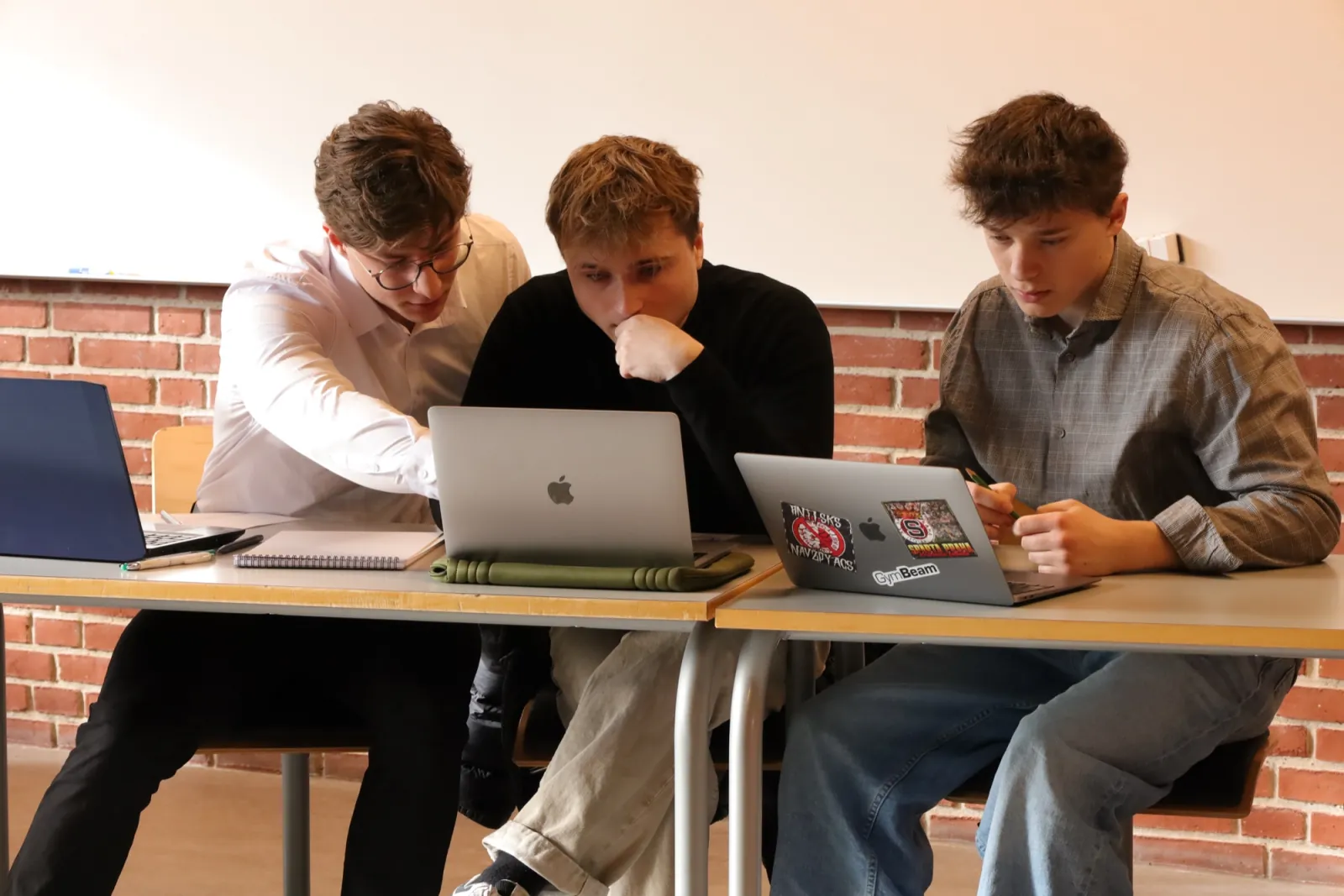 An older student leaning in to help another at a laptop