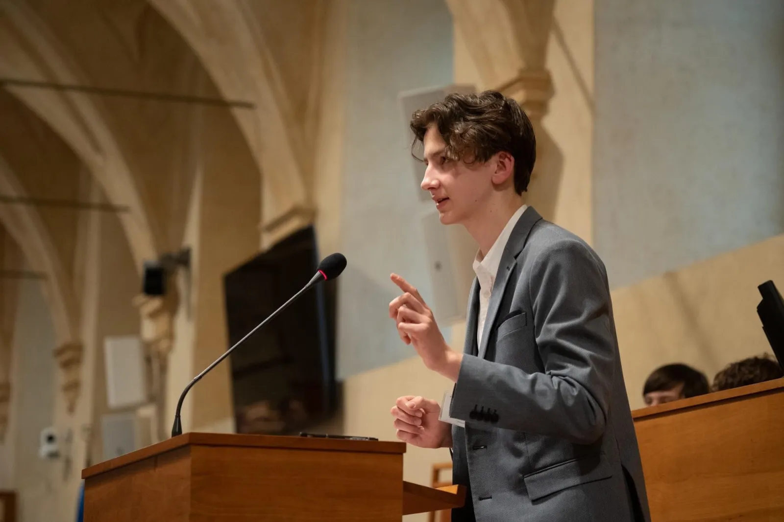 Matyas speaking at a podium in an arched hall