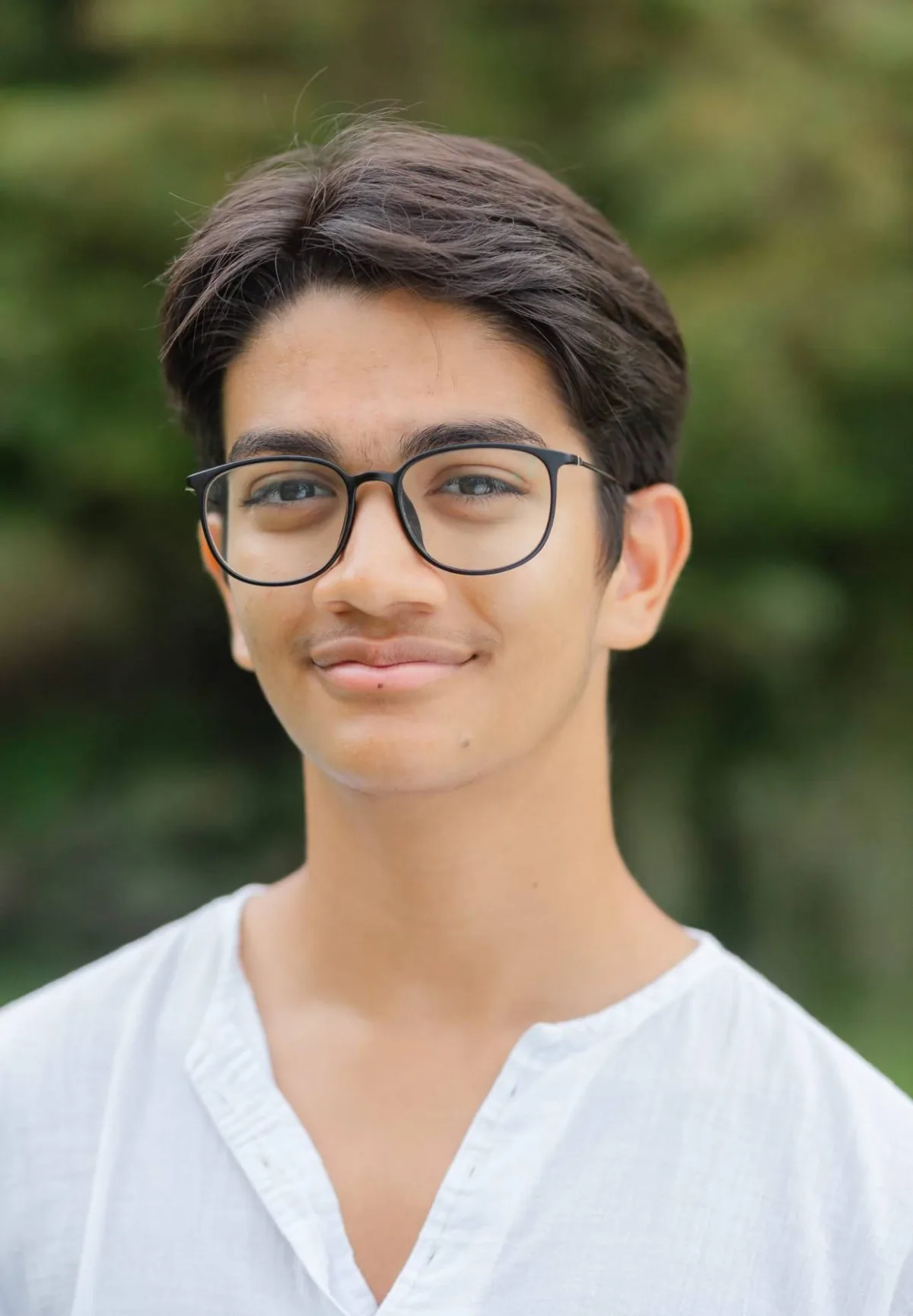 Noah, smiling, in glasses and a white shirt, outdoors